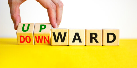 Upward or downward symbol. Businessman turns wooden cubes and changes the word 'downward' to 'upward'. Beautiful yellow table, white background. Business, upward or downward concept. Copy space.