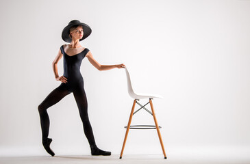 Fototapeta na wymiar young ballerina in black pointe shoes and an elegant hat flies along with chair on gray background