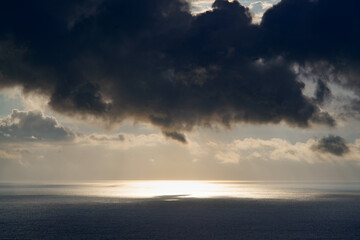The sun breaks through heavy clouds over the sea during a storm