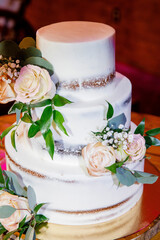 Obraz na płótnie Canvas White wedding cake decorated with white roses and green branches with leaves big white wedding cake with pink roses on an orange table Close up of beautiful modern three-tier wedding cake 