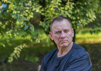 male portrait, handsome mature sexy man with a pensive look, sits in a park against a background of...