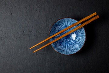 Blue bowl with wooden chopsticks on a black plate