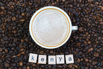 Porcelain and gilded cup of coffee on a background of coffee beans with the inscription Kenya. Production, export and import of coffee