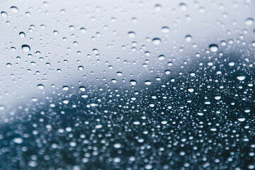 Naklejka na ściany i meble Close up of rain drops on window with dark gray dramatic sky at background.