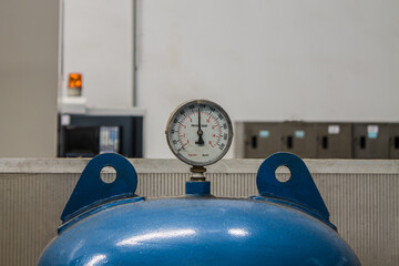 An old rusted analog oil gauge mounted on a blue air tank used to measure air pressure.