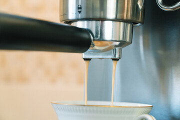 The process of pouring coffee from a coffee machine into a small white porcelain cup with gilding