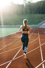 Rear view of Athlete Woman Running Fast at Track in the Morning Light , Training Hard, Getting Ready for Race Competition or Marathon. Fit Girl in Black Sportswear Jogging on a Running Track