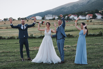 Joyful married couple with their friends having fun in a hayfield on the wedding day