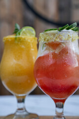 Selective focus on tropical fruit cocktails, a passion fruit daiquiri and a Campari, ron and lime drink, on the white marble table.