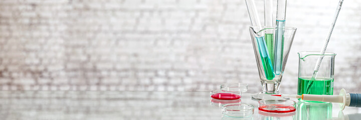 Glass beaker flask cylinder and dropper in chemistry science lin aboratory grey wall background.
