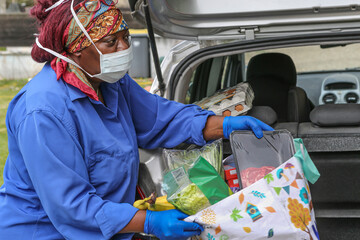 Woman wearing a mask to get her grocery shopping out of her car during covid-19.