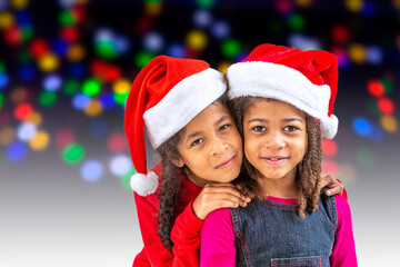 Happy little girls on santa hats against blurred festive bokeh lights. christmas celebration.