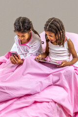 Little girls using digital tablet and smartphone playing in bed. with pink linen.