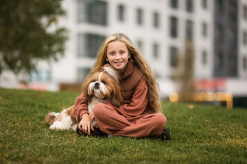 Portrait of beautiful preteen girl petting and hugging shih tzu dog outdoors.