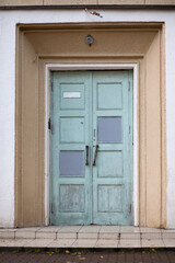 An old wooden blue shabby door to the entrance of a multi-storey residential building.