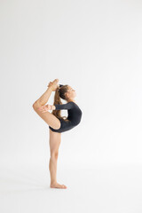 slim artistic teenager girl in black leotard trains on white background in rhythmic gymnastic...