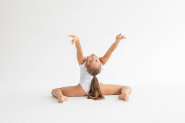 slim artistic teenager girl in white leotard trains on white background in rhythmic gymnastic...