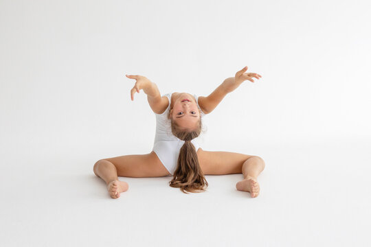 slim artistic teenager girl in white leotard trains on white background in rhythmic gymnastic exercise, children's professional sports