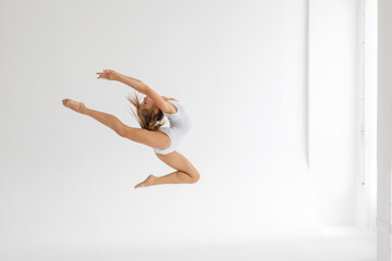 slim artistic teenager girl in white leotard trains on white background in rhythmic gymnastic exercise, children's professional sports - obrazy, fototapety, plakaty