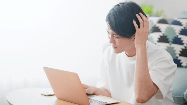 悩みながらノートパソコンを使う男性