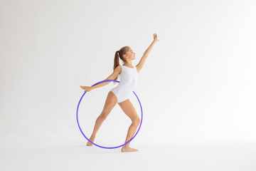 slim artistic teenager girl in white leotard trains on white background with hoop in her hands in rhythmic gymnastic exercise, children's professional sports © klavdiyav