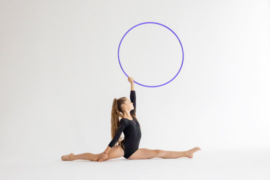 slim artistic teenager girl in black leotard trains on white background with hoop in her hands in rhythmic gymnastic exercise, children's professional sports