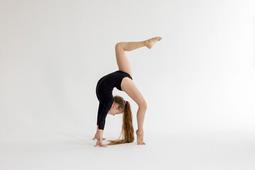 slim artistic teenager girl in black leotard trains on white background in rhythmic gymnastic...