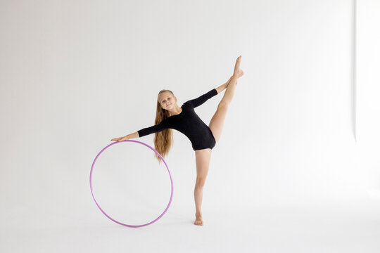 slim artistic teenager girl in black leotard trains on white background with hoop in her hands in rhythmic gymnastic exercise, children's professional sports