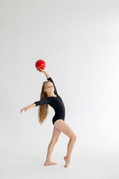 slim artistic teenager girl in black leotard trains on white background with red ball in her hands in rhythmic gymnastic exercise, children's professional sports