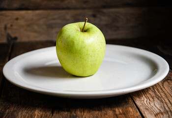 One green apple on a white ceramic plate, on a wooden table.
