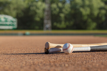 Low angle view of a baseball and bats on dirt infield of baseball park in afternoon sunlight