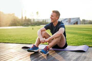 athletic sportsman resting after sport in the park and looking far away at the sunset and smiling