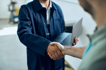 Close-up of maintenance engineer shakes hands with customer at car workshop.