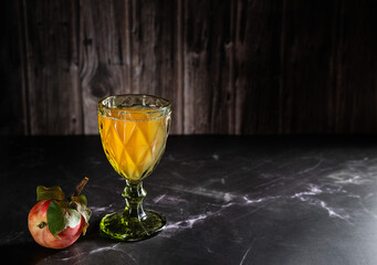Natural, apple juice in a green wine glass and a fresh, red apple with leaves on a dark background. Copy space.
