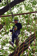 Naklejka na ściany i meble A teenage guy climbs a hanging ladder in a rope amusement park