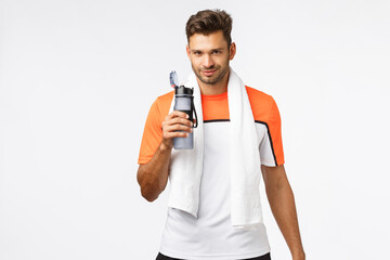 Handsome sportsman with bristle, wear activewear, towel over neck, holding bottle, drink water with satisfied smiling expression, finish good endurance practice, football player rest after match - Powered by Adobe
