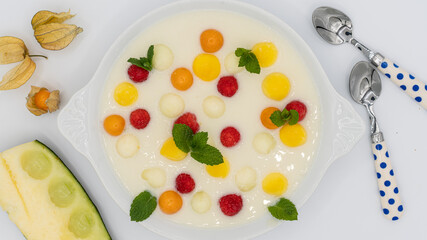 Cold melon cream with pieces of melon, raspberries, mango, physalis peruviana and mint leaves on a white background.
