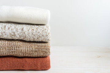 Fototapeta na wymiar A stack of folded knitwear in white, beige and brown on a light background, copy space.