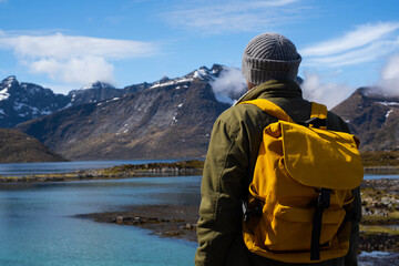 Guy travels with a yellow backpack through picturesque places with beautiful mountain landscapes.