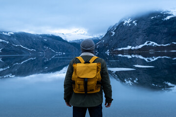 Fototapeta na wymiar Guy travels with a yellow backpack through picturesque places with beautiful mountain landscapes.