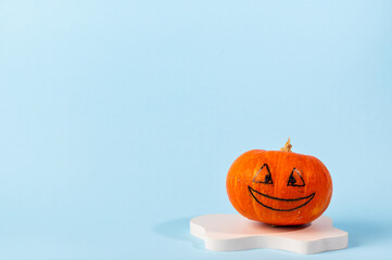 Small orange carved pumpkin on blue background with copy space. Concept celebration of Halloween or Thanksgiving. Cosmetics podium for halloween. Autumn still life.