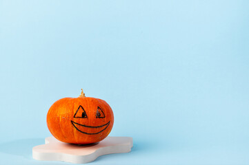 Small orange carved pumpkin on blue background with copy space. Concept celebration of Halloween or Thanksgiving. Cosmetics podium for halloween. Autumn still life.