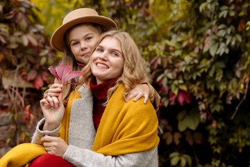 Fototapeta premium A young adult blonde mother with a 7-year-old daughter on a walk in the autumn park hug and laugh 