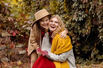 A young adult blonde mother with a 7-year-old daughter on a walk in the autumn park hug and laugh
