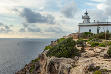 Fototapeta na wymiar Cap Blanc lighthouse on the rocky coast of the island of Mallorca. In the background s seascape of the Mediterranean Sea at sunset with clouds. Sublime landscape