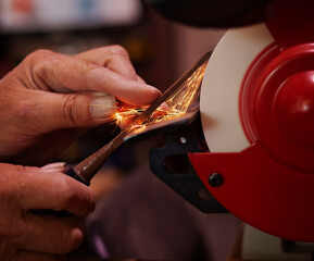 A pair of skilled mans hands sharpening a woodworking chisel on a bench grinding wheel.