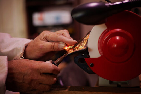 A pair of skilled mans hands sharpening a woodworking chisel on a bench grinding wheel. - Powered by Adobe