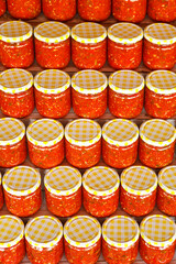 Several rows of glass jars with canned appetizer of tomatoes with horseradish, put up for sale.