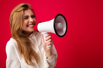 Photo portrait of beautiful attractive positive happy smiling dark blonde young woman with sincere emotions wearing stylish white hoodie isolated over red background with copy space and shouting into