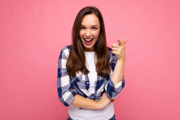 Shot of young happy smiling beautiful brunette woman with sincere emotions wearing trendy check shirt isolated on pink background with empty space